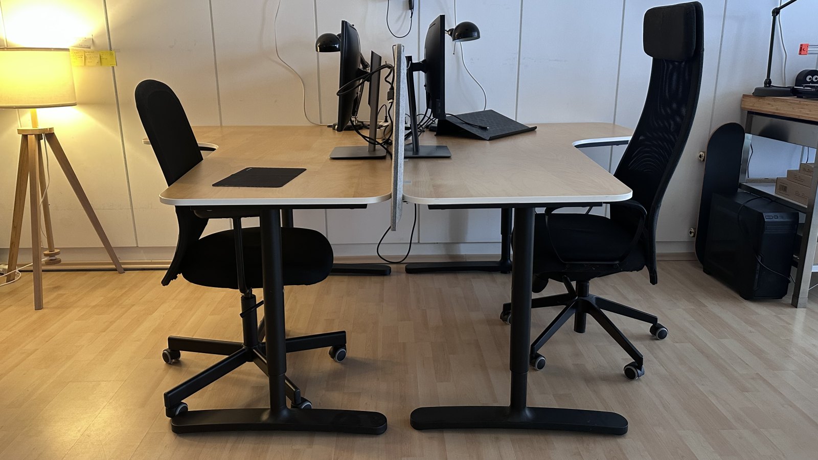 Zwei Schreibtische im offenen Arbeitsbereich, jeweils mit Monitor, Tischleuchte und Bürostuhl, dazwischen ein Filz-Sichtschutz.